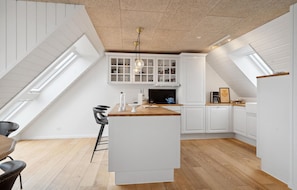A modern kitchen with white cabinetry, a wooden countertop, and a central island. There are two black chairs and a blue kettle on the island.