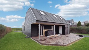Una casa moderna con techo inclinado, un porche cubierto y una terraza de madera.