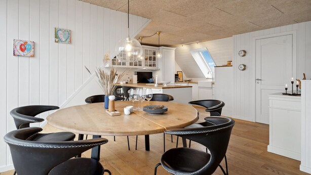 Una cocina moderna con armarios blancos, una mesa de comedor redonda de madera, sillas negras e iluminación colgante.