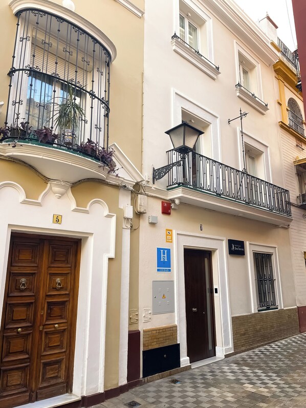 A building with a wooden door, a balcony with plants, and a sign indicating a public restroom.