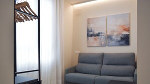 Un salon moderne avec un canapé gris, une petite table d’appoint noire et des tableaux abstraits accrochés au mur.