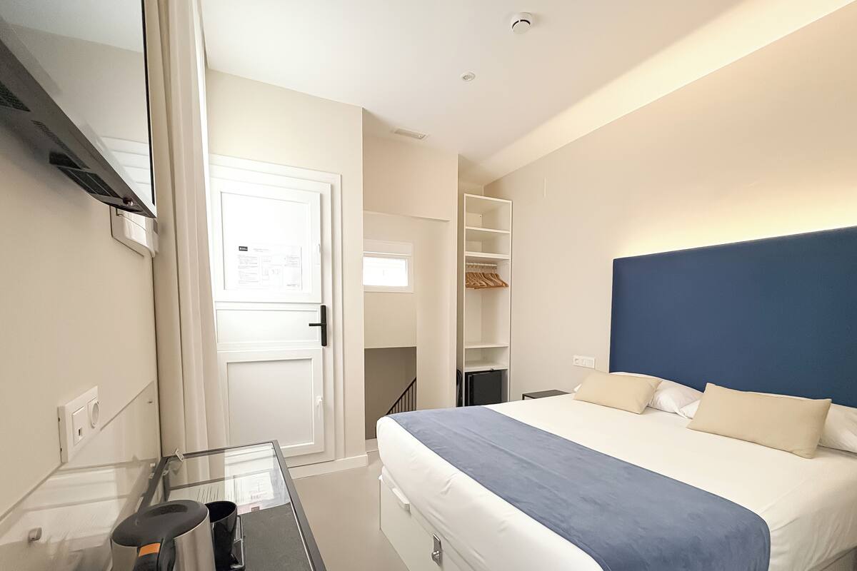 Quarto de hotel com cama, escrivaninha com cafeteira, guarda-roupa e espelho.