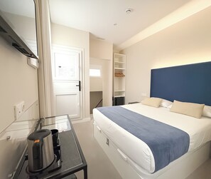 A hotel room with a bed, a desk with a coffee maker, a wardrobe, and a mirror.