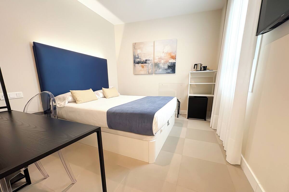 Quarto de hotel moderno com cama, escrivaninha e televisão.