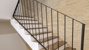 Un escalier avec des rampes noires et des marches en bois, adossé à un mur à la texture particulière.