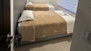 A bedroom with two beds, a window with blinds, and a door. - Cozy apartment near to the center. (Guatavita)
