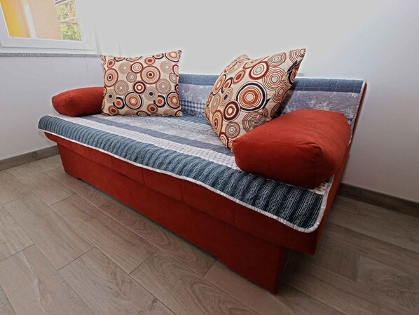 Um sofá vermelho com almofadas estampadas e um cobertor listrado.