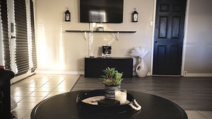 A living room with a black round table, a flat-screen TV mounted on the wall, a black console table, and a door with a decorative handle. - Welcome to the River House! Bright peaceful desert/river home.  (Parker)