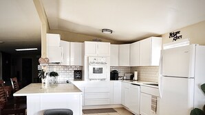 A modern kitchen with white cabinets, a central island, a refrigerator, and a coffee maker. - Welcome to the River House! Bright peaceful desert/river home.  (Parker)