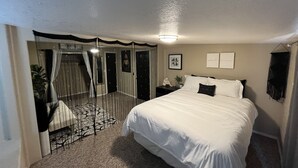 A bedroom with a large bed, a nightstand, a wall-mounted light, a framed picture, and a curtain. - Welcome to the River House! Bright peaceful desert/river home.  (Parker)