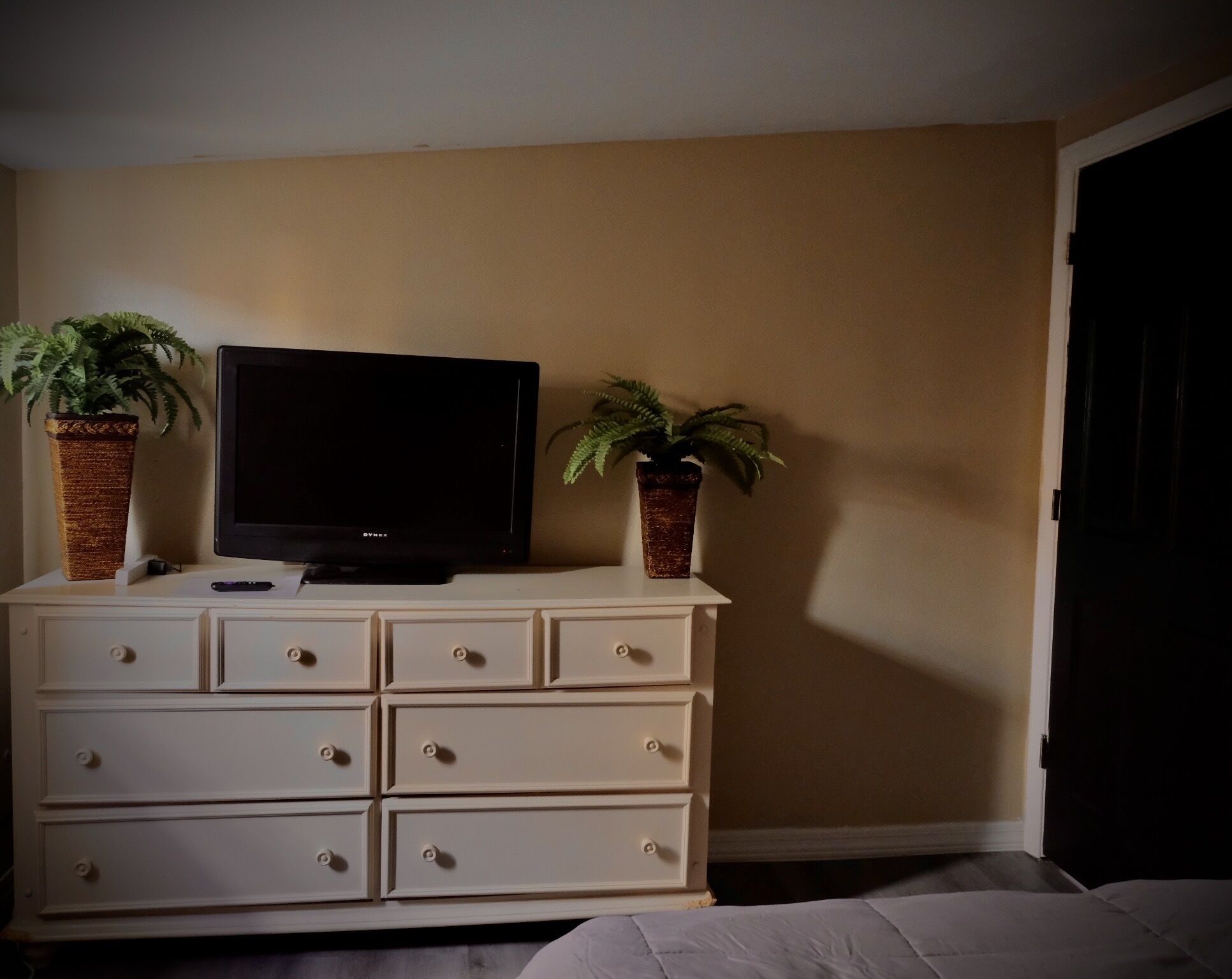 A room with a TV on a dresser, two potted plants, and a door.