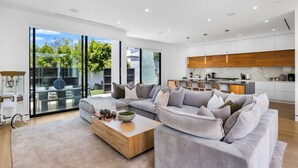 A modern living room with a sectional sofa, a coffee table, and a view of the kitchen. - Pool, spa, rooftop, back yard, gym, fire pit, games and more (Los Angeles)