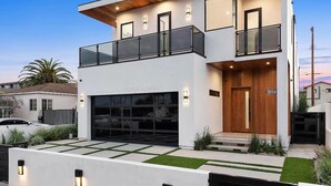 A modern two-story house with a garage, a balcony, and a well-lit entrance. - Pool, spa, rooftop, back yard, gym, fire pit, games and more (Los Angeles)