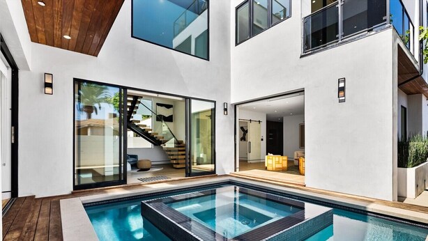 A modern house with a central swimming pool, glass doors leading to a living area, and a staircase. - Pool, spa, rooftop, back yard, gym, fire pit, games and more (Los Angeles)
