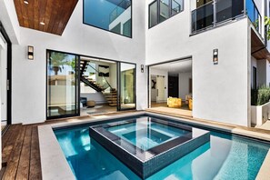 Ein modernes Haus mit einem zentral gelegenen Schwimmteich, Glastüren zu einem Wohnbereich und einer Treppe.