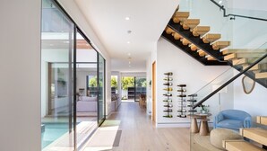 A modern interior with a staircase, a wine rack, and a glass door leading to an outdoor area. - Pool, spa, rooftop, back yard, gym, fire pit, games and more (Los Angeles)