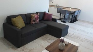 Un salon moderne avec un canapé d’angle foncé, une table basse en bois et un coin repas avec une cuisine en arrière-plan.