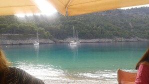 Vue d’une baie paisible où deux voiliers sont amarrés près du rivage, le tout étant entouré d’une colline boisée.