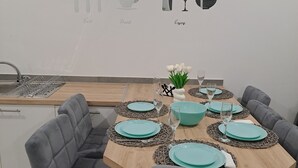Un coin repas avec une table en bois dressée pour quatre personnes, des chaises à revêtement gris et une cuisine en arrière-plan.