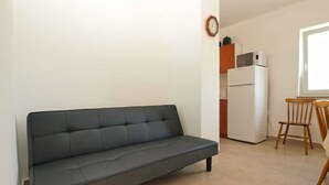 Ein kompakter Wohnbereich mit Sofa, einer kleinen Küchenzeile inklusive Kühlschrank und Mikrowelle sowie einem Fenster für natürliches Licht.