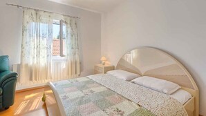 Ein Schlafzimmer mit einem Bett, einem Nachttisch mit Lampe, einem Sessel und einem Fenster mit Vorhängen.