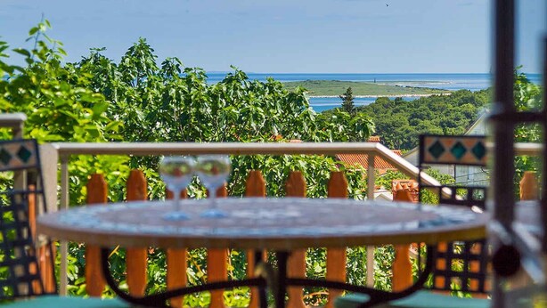 Eine Terrasse mit Tisch und Stühlen mit Blick auf eine Küstenlandschaft mit Bäumen und dem Meer.
