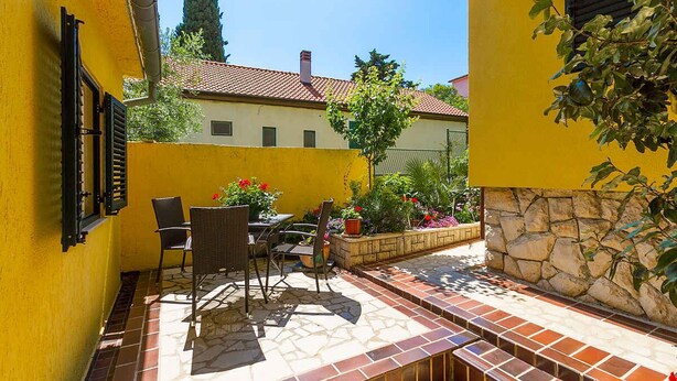 Ein gelbes Gebäude mit einer gefliesten Terrasse, Gartenmöbeln und Blumentöpfen.