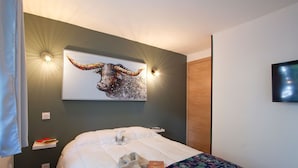 A bedroom with a bed, a wall-mounted artwork of a bull, and a television on the wall.