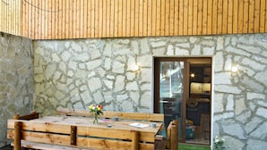A wooden bench with a vase of flowers, set against a stone wall with a wooden slatted roof.