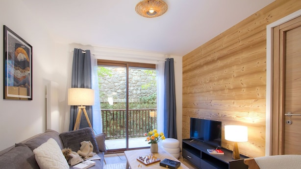 A modern living room with a sofa, coffee table, TV, and a balcony with a stone wall and greenery.