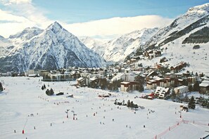 A snow-covered mountain town with ski slopes, buildings, and a prominent peak in the background.