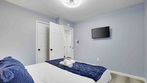 Un dormitorio con una cama, un televisor en la pared y una puerta.