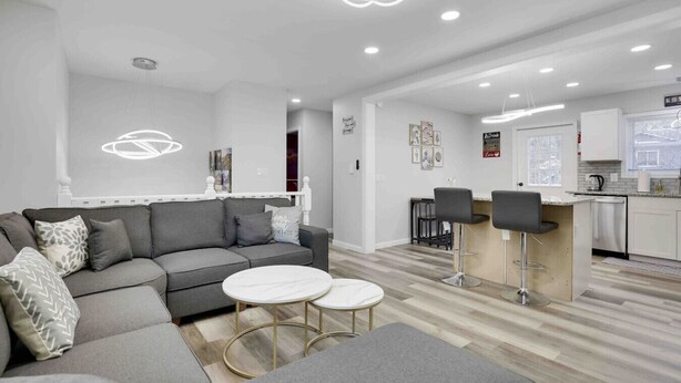 Una sala de estar moderna con un sofá gris, dos mesas redondas y una cocina con barra.