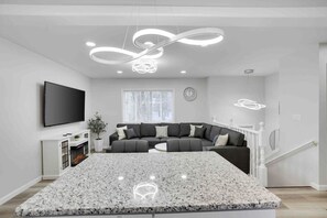 Uma sala de estar moderna com um amplo sofá em formato de L, uma TV de tela plana na parede e um lustre de design exclusivo.