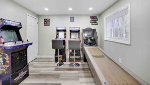Un pasillo con juegos de arcade, un banco de madera y una ventana con persianas.