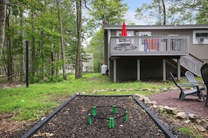 A backyard with a raised garden bed, a deck with outdoor seating, and a building in the background. - Cozy Hot Tub 4BR Poconos Home Near All Attractions (Tobyhanna)