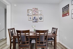 A dining area with a wooden table and four chairs, a vase with flowers, and a wall with framed artwork and a sign. - Cozy Hot Tub 4BR Poconos Home Near All Attractions (Tobyhanna)