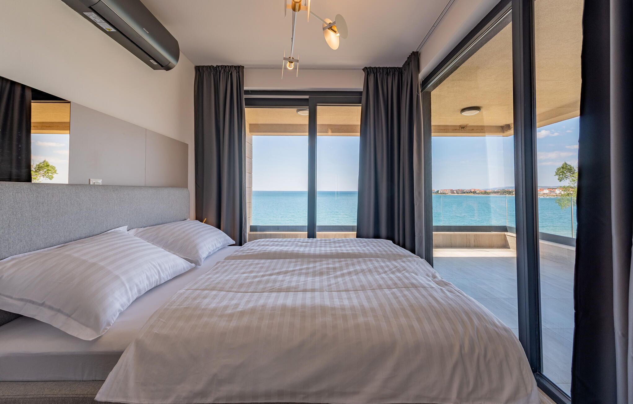 Une chambre d’hôtel moderne avec un grand lit, un ventilateur de plafond et une vue sur la mer.