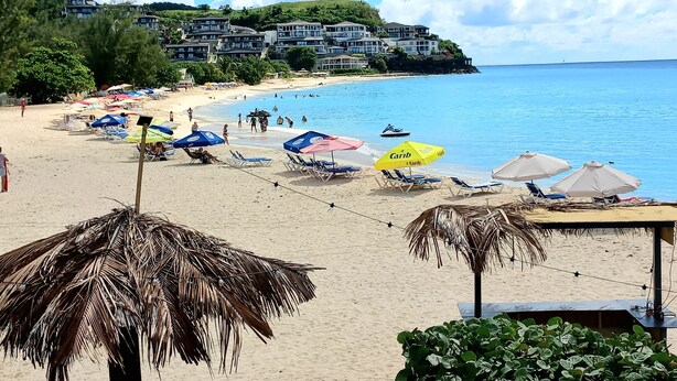 A beach with umbrellas, lounge chairs, and a view of a hill with buildings. - A Blissful Carib/n Getaway! Work or Leisure, 15 mins to Beaches & Restaurants. (Saint John's)