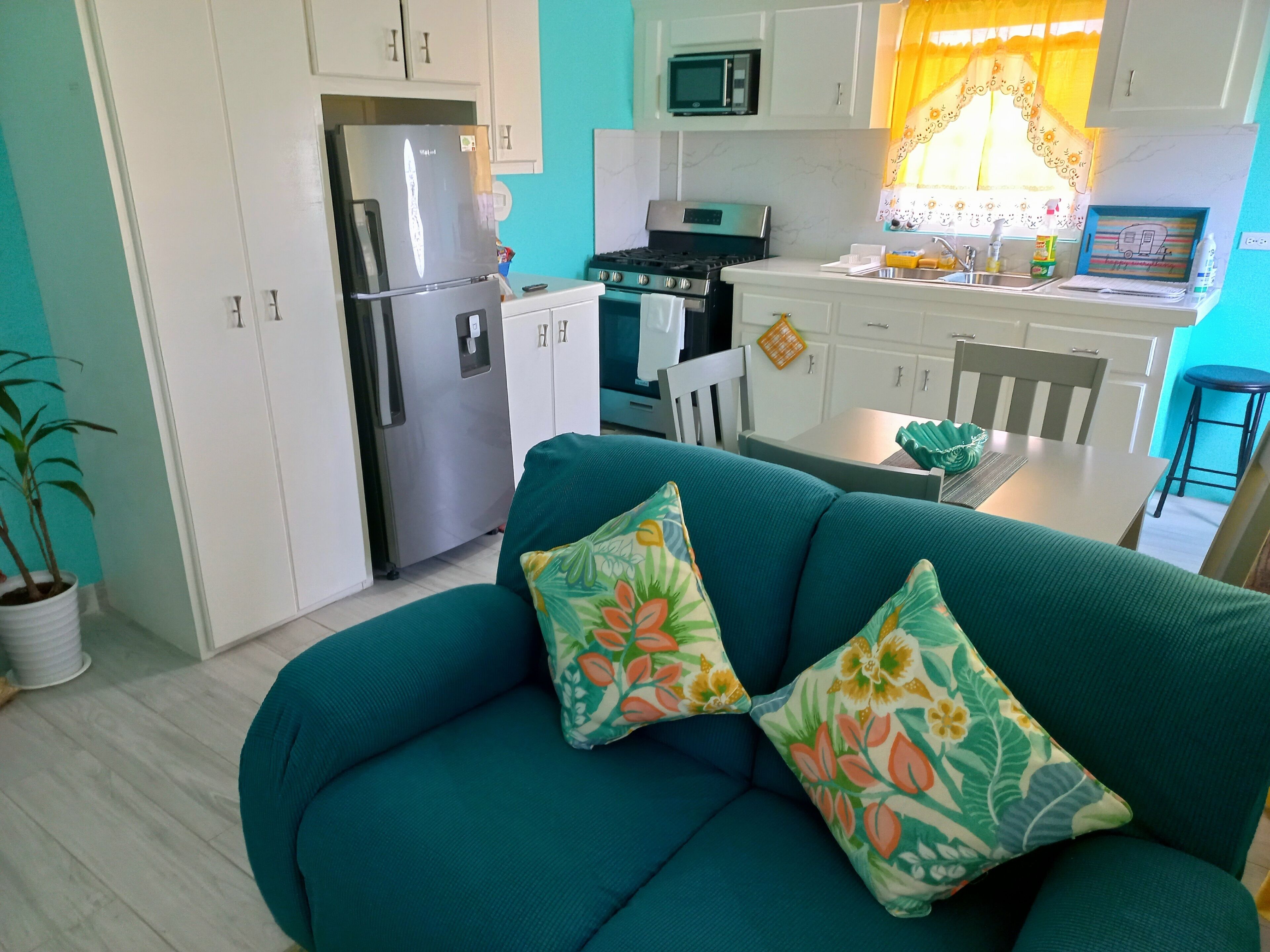 A compact living space with a teal sofa, a refrigerator, a microwave, and a dining area with a table and chairs.