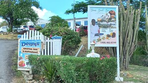 A sign for Dennis' Cocktail Bar & Restaurant with a stone wall and greenery. - A Blissful Carib/n Getaway! Work or Leisure, 15 mins to Beaches & Restaurants. (Saint John's)