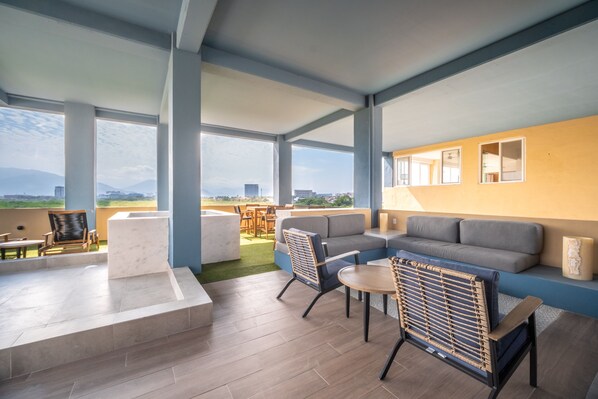 A rooftop lounge with a sofa, chairs, and a table, overlooking a cityscape.