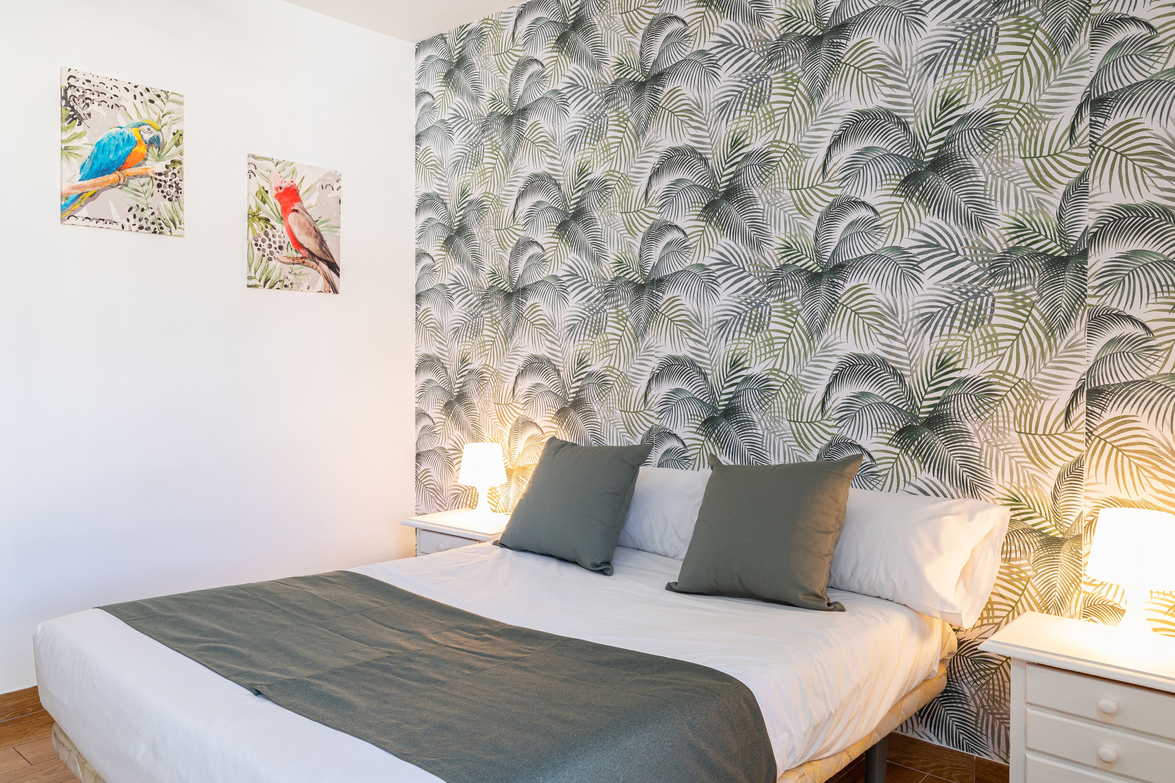 Ein Schlafzimmer mit Bett, Kissen, Nachttisch und Wandbildern.