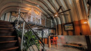 Un loft espacioso con techo alto, un entrepiso, una escalera y un comedor con sillas rojas.