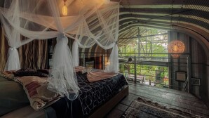 Un dormitorio con cama con dosel, vistas al verdor exterior y una estructura de techo curva singular.