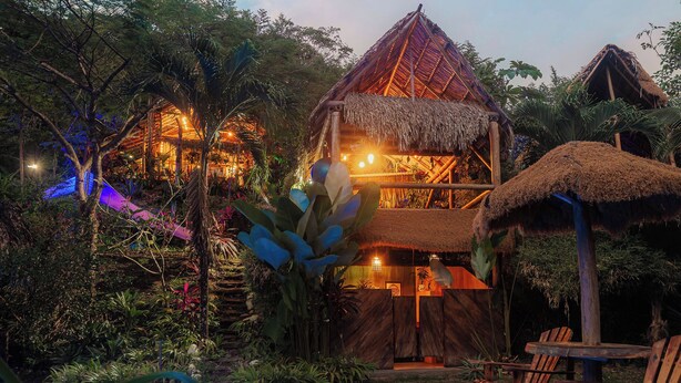Un edificio de techo de paja con varios niveles, rodeado de exuberante vegetación tropical.