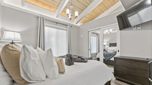 A modern hotel room with a large bed, a wooden ceiling, a flat-screen TV, and a dresser.