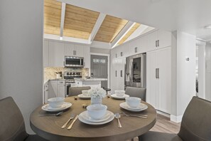A modern kitchen with white cabinetry, stainless steel appliances, and a dining area with a round table set for four. - Peak Comfort in North Tahoe! Elevate Your Stay with Our Premium Retreat.  (Incline Village)