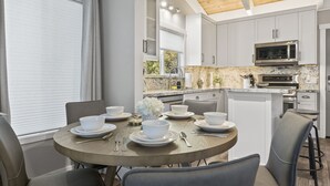 A modern kitchen with white cabinets, a wooden ceiling, and a dining area with a round table set for four.