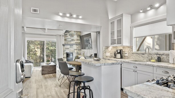 A modern kitchen with a stone backsplash, a large island with bar stools, and a dining area with a view of the outdoors.